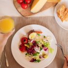 A top-view of a delicious breakfast setting featuring a salad, bread, cheese, tomatoes, and orange juice.