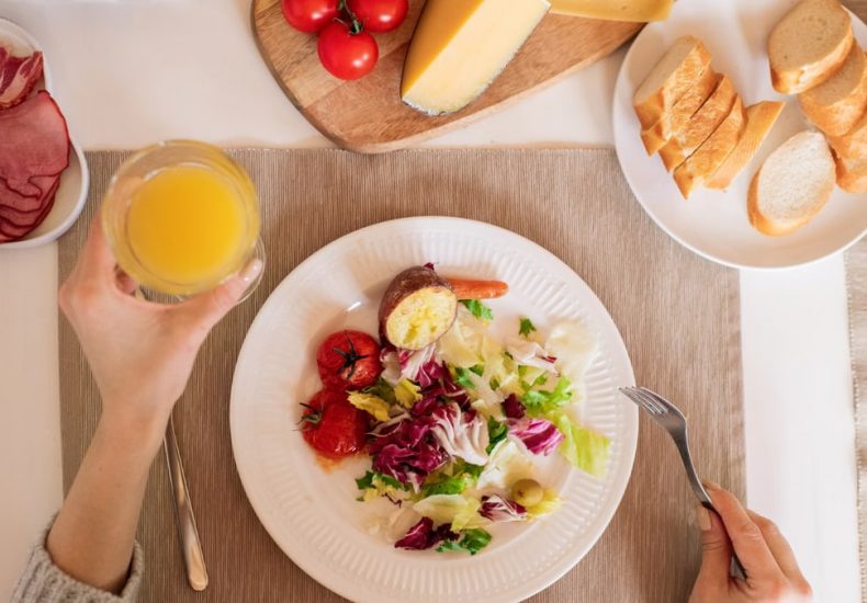 A top-view of a delicious breakfast setting featuring a salad, bread, cheese, tomatoes, and orange juice.